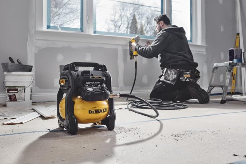 DEWALT cordless compressor in a room under renovation, worker using nail gun near window.