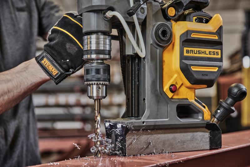 Person uses DEWALT brushless magnetic drill to bore holes in metal, creating metal shavings on a workshop table.