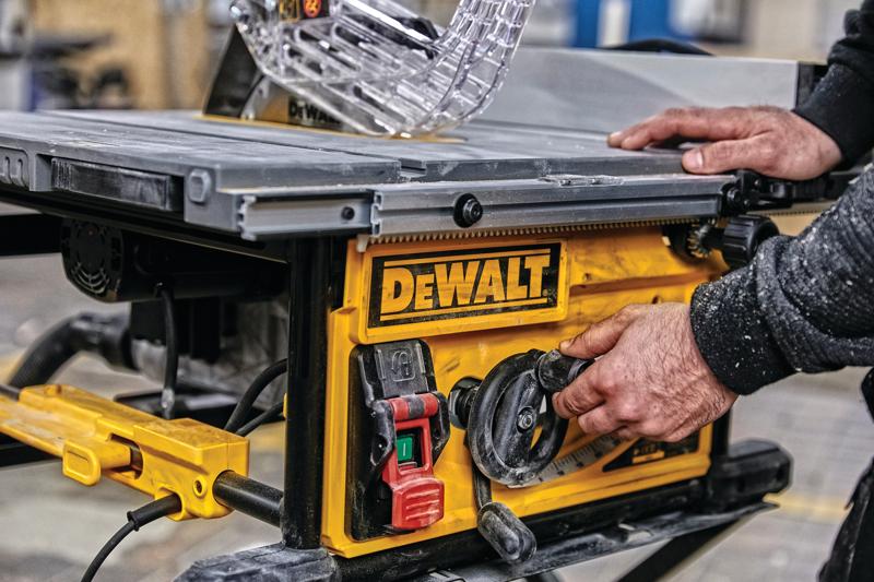 Close-up of a person adjusting the settings on a DEWALT table saw, featuring a yellow control panel with switches and dials in a workshop setting.