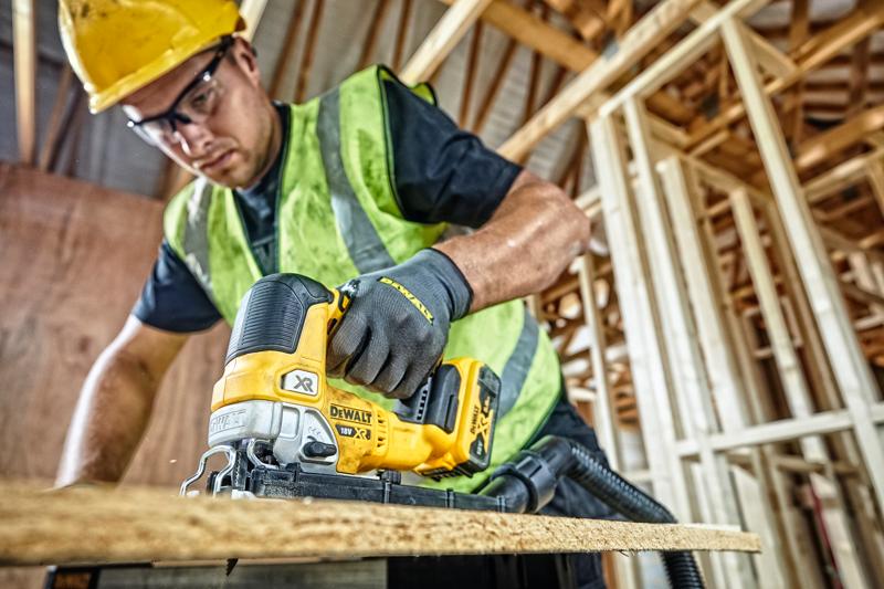 DEWALT DCS334P2 jigsaw used for cutting wood at a construction site by a worker wearing safety gear.