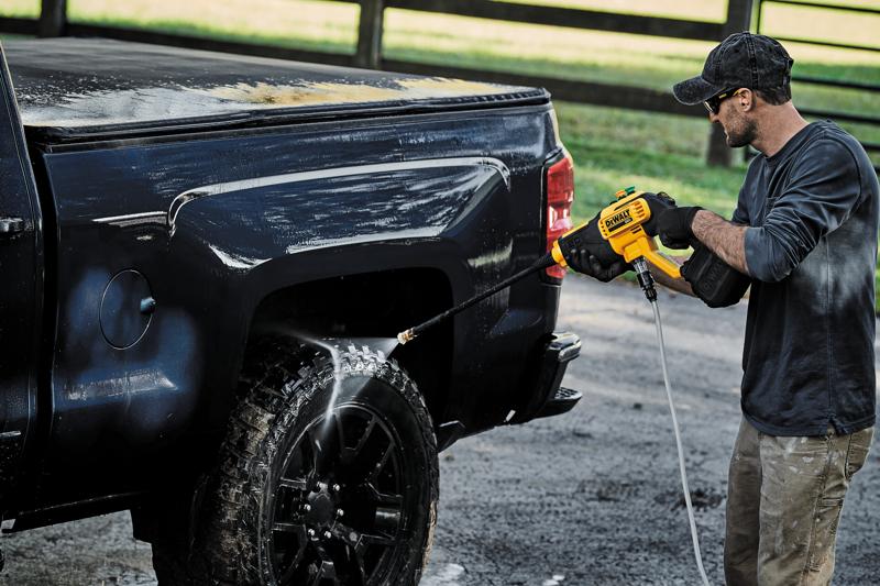 Osoba používá bezdrátový tlakový čistič DEWALT DCPW550B k čištění kola a boku černého pickupového trucku venku.