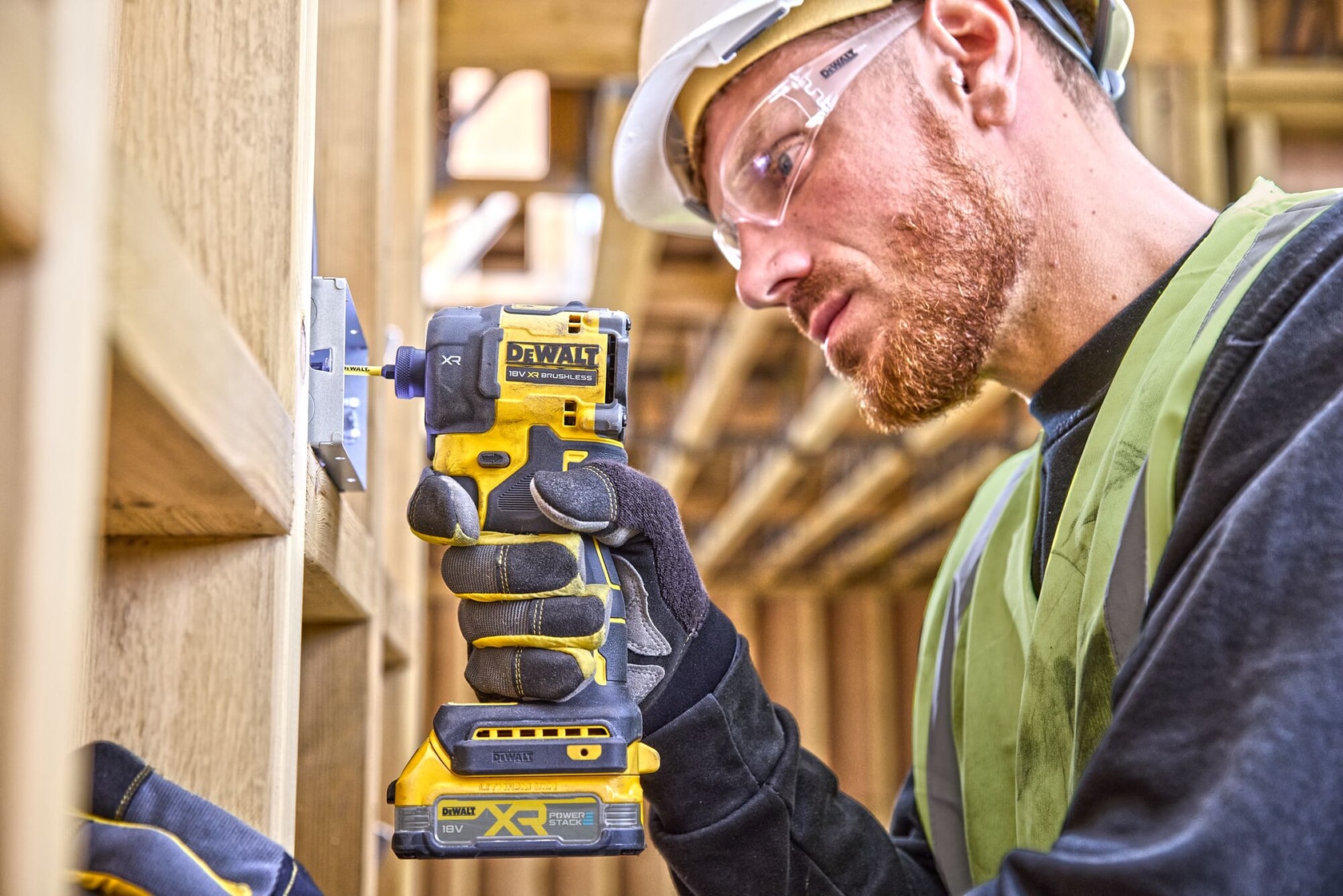 Worker uses a DEWALT DCF870NT cordless impact driver on a wooden structure at a construction site.